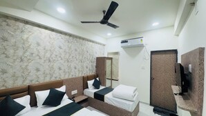 Habitación de hotel con dos camas, ventilador de techo, aire acondicionado, espejo y televisor sobre un soporte de madera.