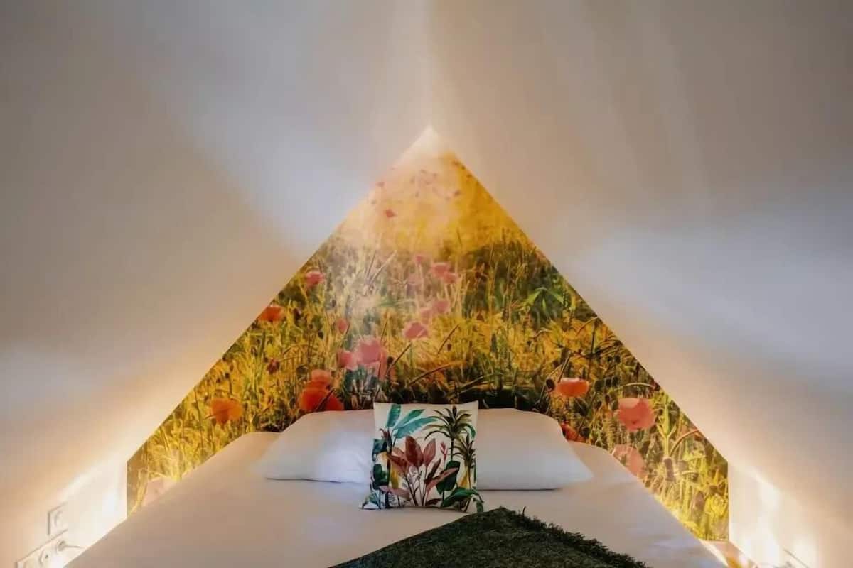 Una cama con un cojín floral y un mural en la pared de un campo.