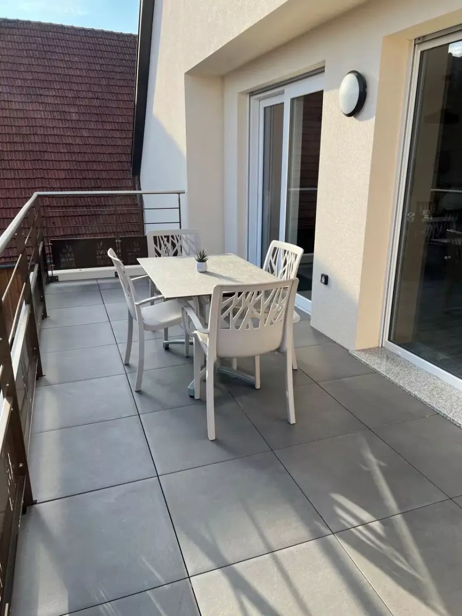 A balcony with a white table and chairs, a small potted plant, and a sliding glass door.