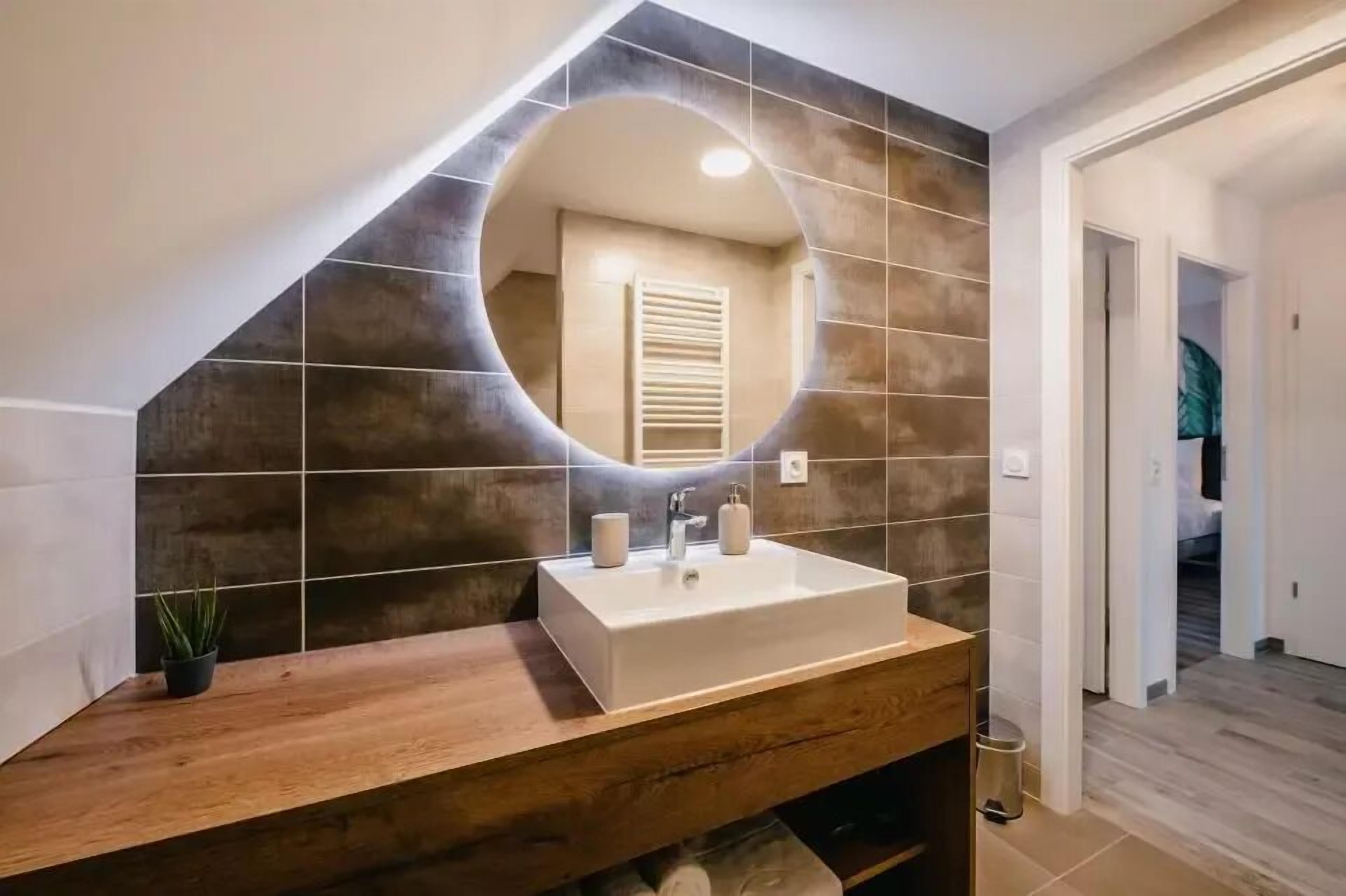 A bathroom with a large mirror, a wooden vanity, and a tiled wall.