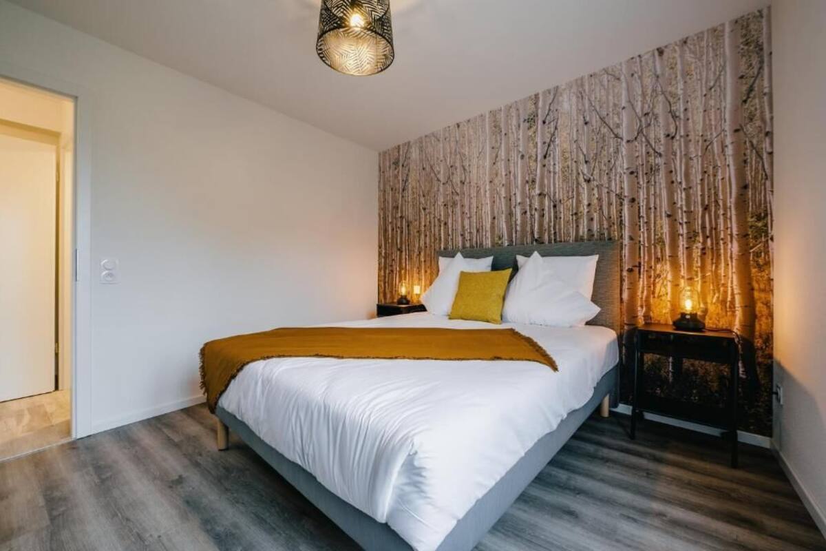 Un dormitorio con cama, mesita de noche, lámpara de pared y una puerta.