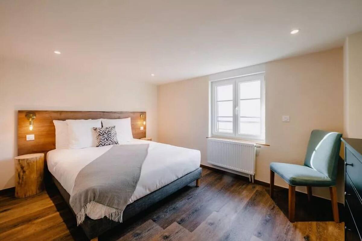 Un dormitorio con cama, una silla, cómoda y ventana con luz natural.