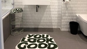 Un baño con un lavabo blanco, un espejo y una pared verde. Hay un bote de basura negro y un inodoro blanco.