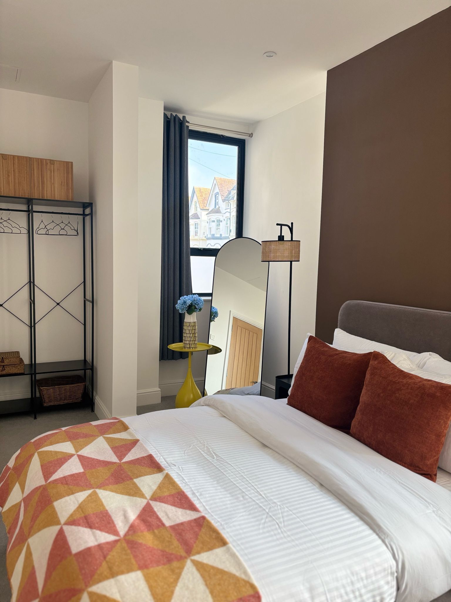 Habitación de hotel con cama, armario, espejo y ventana con vistas a edificios.