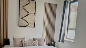Un dormitorio con cama, una obra de arte en la pared, persianas verticales y una ventana con cortinas.
