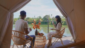 Two people seated at a table with a view of a lake and greenery, inside a tent-like structure. - La Vela Legacy Resort (Hue)