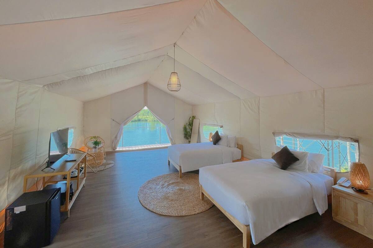 A tented accommodation with two beds, a desk, and a computer.