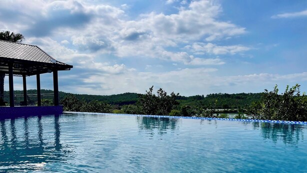 A clear blue pool with a covered seating area and a view of a forested hill in the background. - La Vela Legacy Resort (Hue)