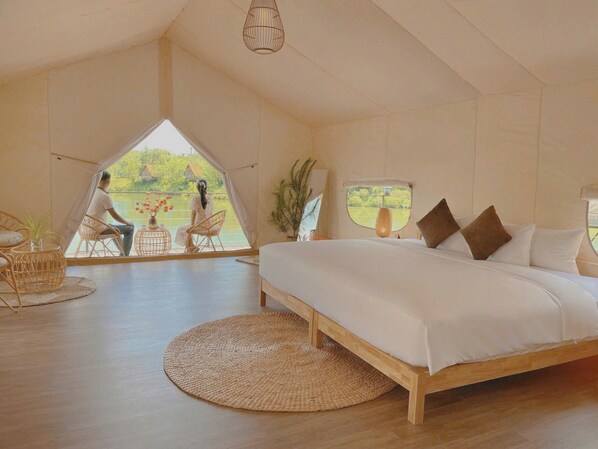 Une chambre avec un grand lit, une vue sur l’extérieur, des meubles en osier et un luminaire suspendu.