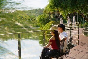 A couple seated on a bench overlooking a lake with a bridge and trees in the background. - La Vela Legacy Resort (Hue)