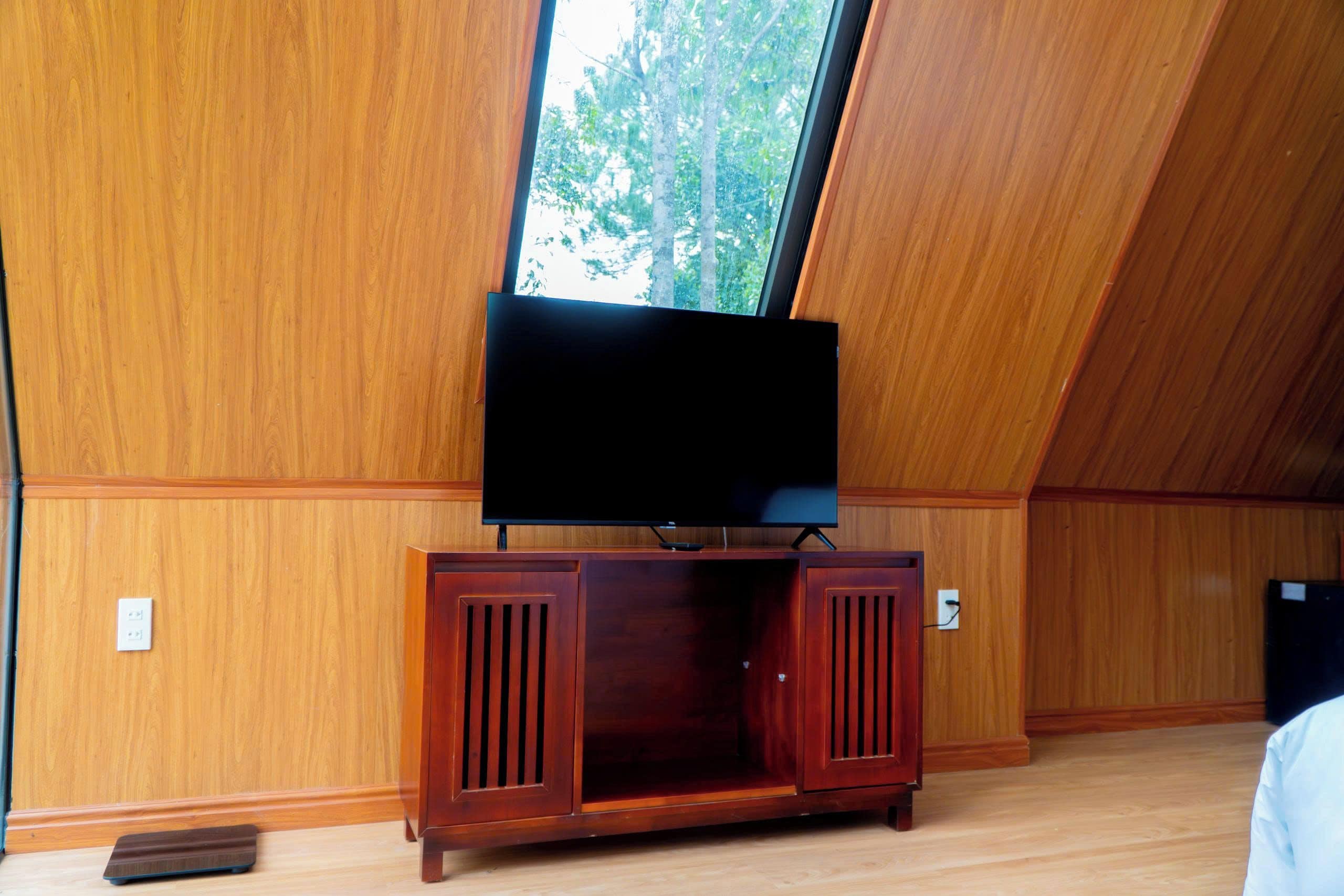 Una habitación con un revestimiento de madera, un televisor sobre un mueble de madera y una ventana con vistas a árboles.