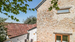 A stone building with a tiled roof, a small window, and a patio with outdoor furniture. - Newlands Barn (Wellington)
