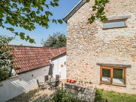 A stone building with a tiled roof, a small window, and a patio with outdoor furniture.