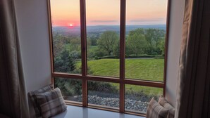 A room with a large window offering a view of a sunset over a green landscape. - Newlands Barn (Wellington)