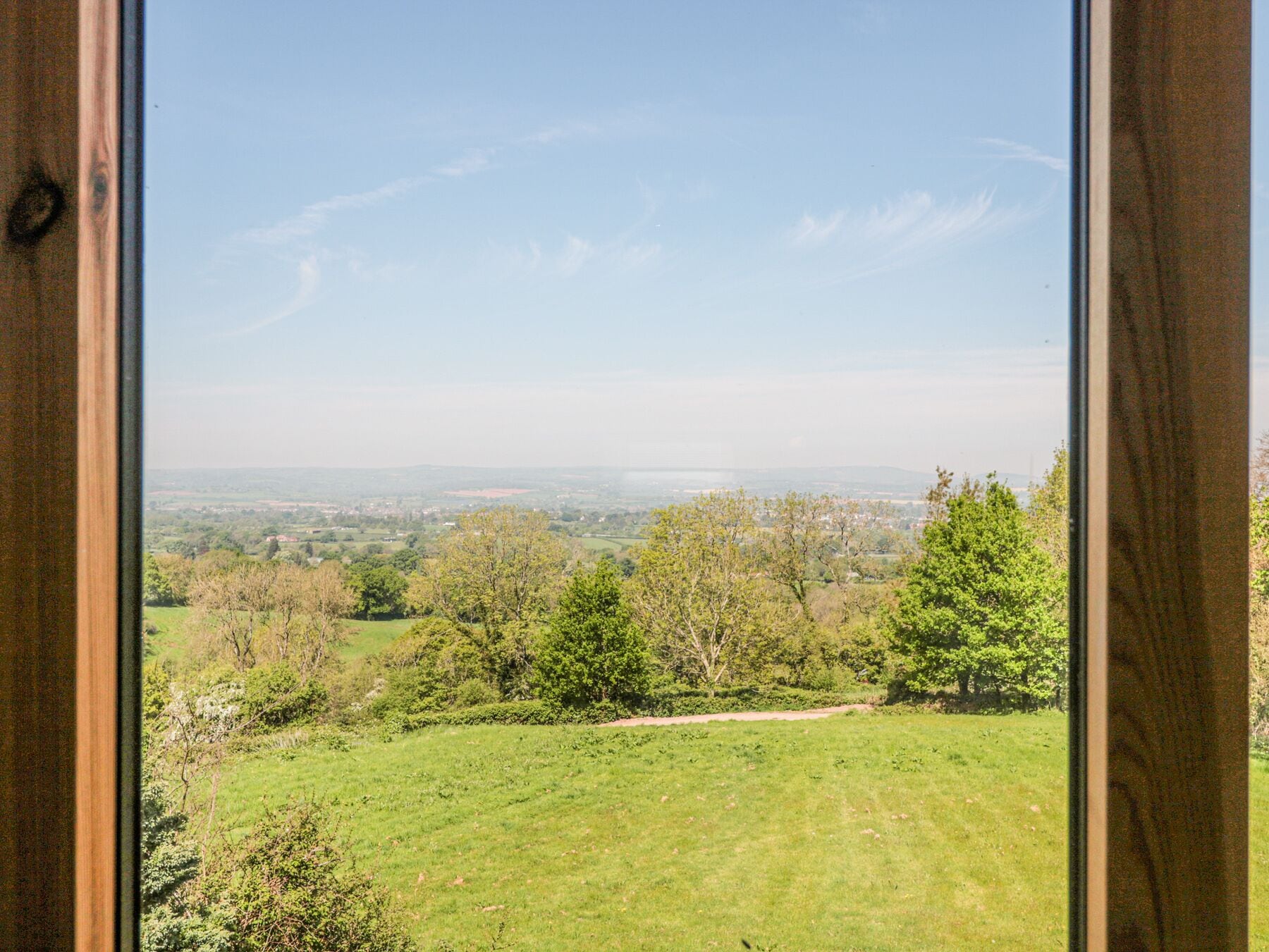 Blick durch ein Fenster auf ein grasbewachsenes Feld mit Bäumen und eine ferne Landschaft.
