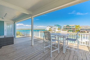 A wooden deck with a table and chairs, overlooking a waterfront with buildings.