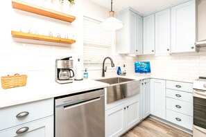 A modern kitchen with white cabinetry, a stainless steel dishwasher, and a coffee maker.