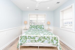 A bedroom with a bed, two bedside tables, a window with blinds, and a ceiling fan.