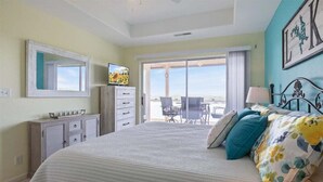 Un dormitorio con cama, cómoda, televisor y balcón con sillas.