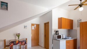 A compact kitchen with wooden cabinets, a microwave, and a refrigerator. There is a dining table with chairs and a small decorative vase.