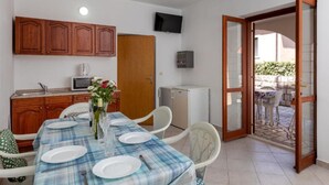 A compact kitchen with wooden cabinets, a microwave, and a small refrigerator. A dining table with a plaid tablecloth is set for four, and a flower vase is on the table.