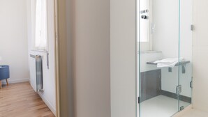 Un baño moderno con cabina de ducha de vidrio, un lavabo blanco y una silla azul.