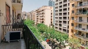 Un edificio residencial con varios balcones, una zona de estacionamiento con coches y un área verde con árboles.