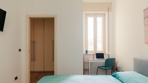 Un dormitorio con una cama, un escritorio con una computadora portátil, una silla y un ventanal.