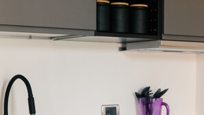 Una cocina moderna con un grifo negro, un portal vasos morado y una campana extractora de acero inoxidable.