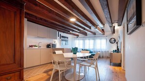 Een moderne keuken met witte kasten, een eethoek met witte stoelen, en zichtbare houten balken aan het plafond.