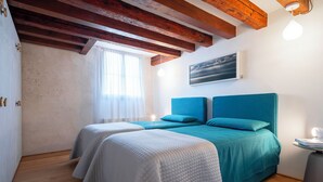 Een slaapkamer met twee bedden, houten balken, een schilderij en een raam met dunne gordijnen.