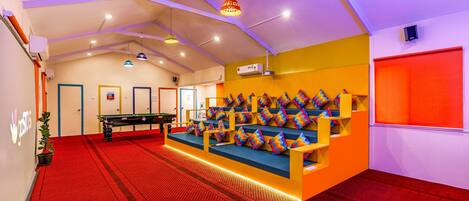 A room with a pool table, a seating area with colorful cushions, and a red carpet.