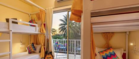 Una habitación con literas, una guitarra y un balcón con vistas a palmeras.