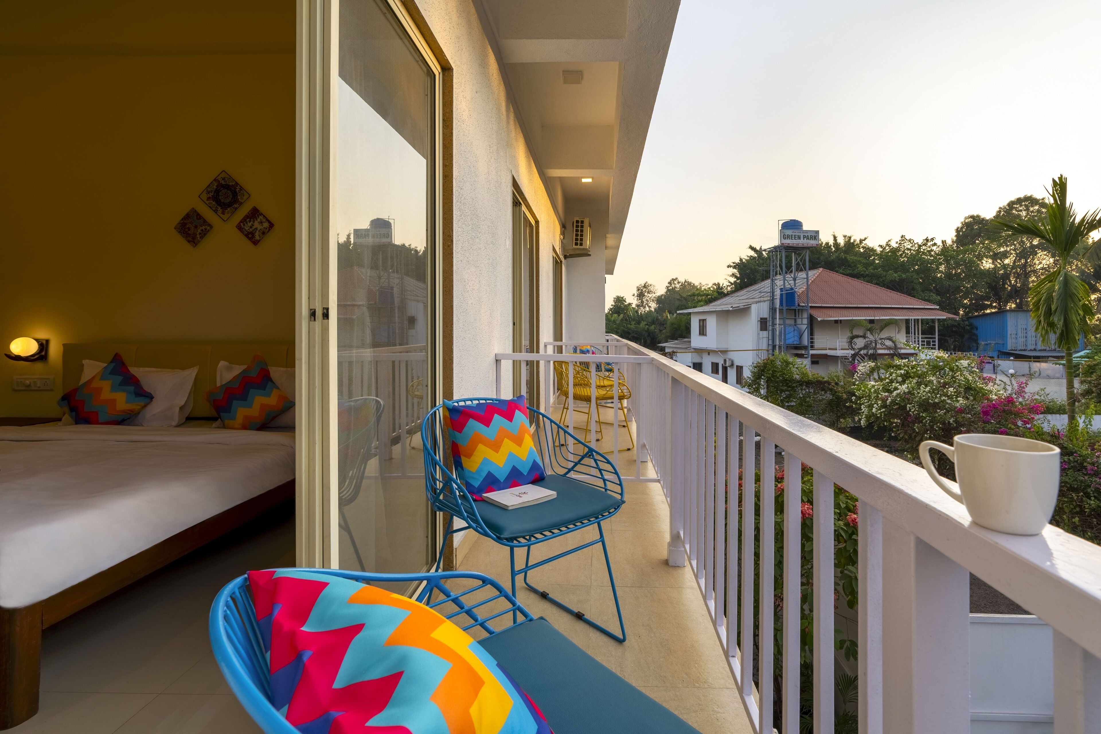 A balcony with a bed, a blue chair with a colorful cushion, and a white railing.