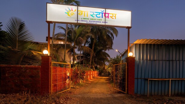 A hotel entrance with a signboard, a gated pathway, and palm trees. - goSTOPS Alibaug (Alibag)