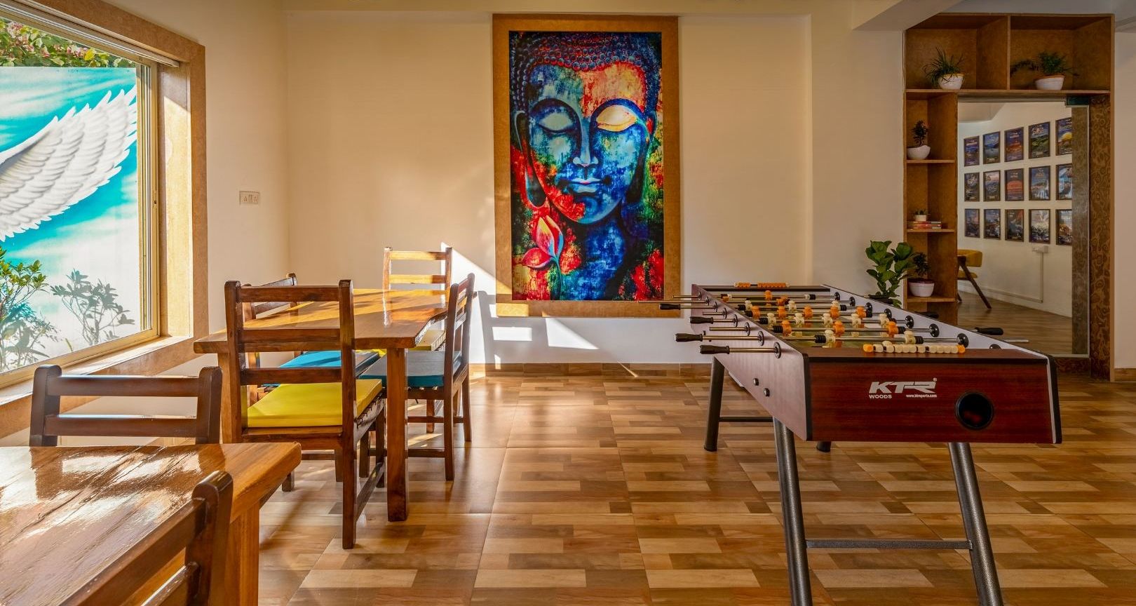 A 24/7 in-house cafe with wooden furniture, a foosball table, and a Buddha painting.