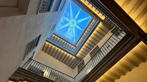 Un ampio atrio con soffitto a volta e lucernario, una scala centrale e vista sul cielo.