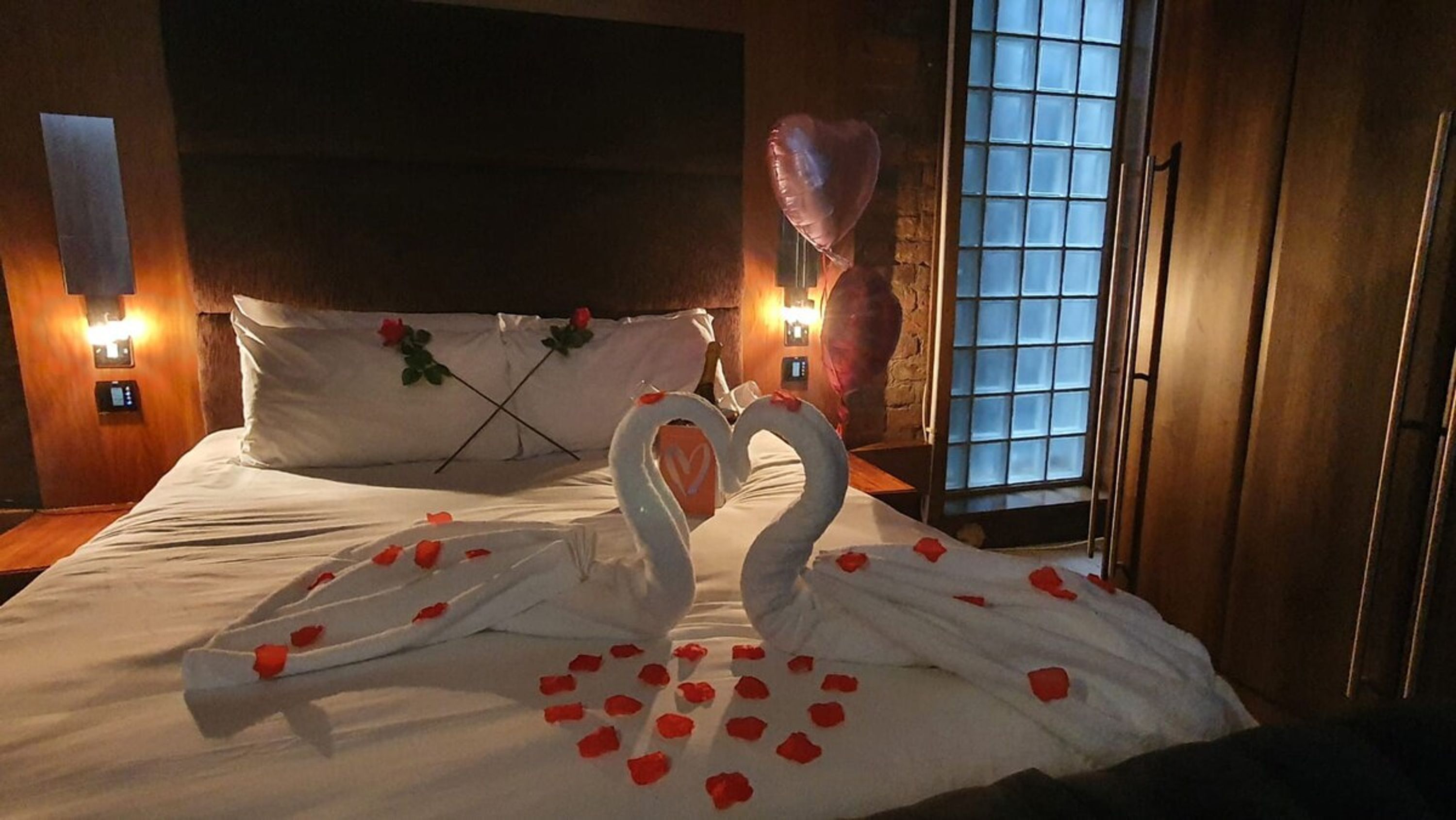 Una habitación de hotel con una cama, una decoración con forma de corazón hecha de pétalos de rosa y un globo.