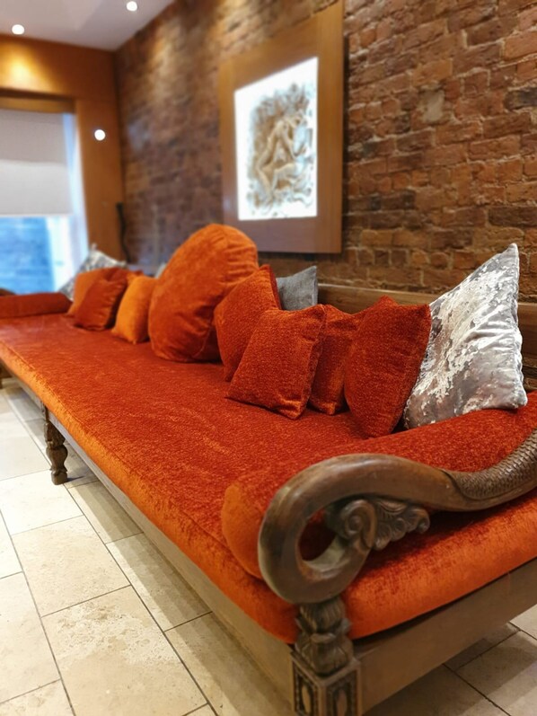 A sofa with orange cushions and a silver pillow, set against a brick wall with a framed artwork above it. - The Famous Floor Sleeps 26 and Group Acc Sleeps30 (Liverpool)