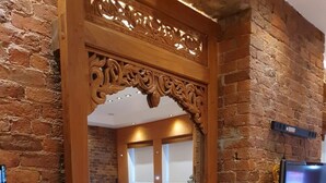 A dining area with a brick wall, a wooden-framed mirror, a TV mounted on the wall, and a table with chairs. - Infinity Partypadsliverpool Hen and Stag Welcome (Liverpool)