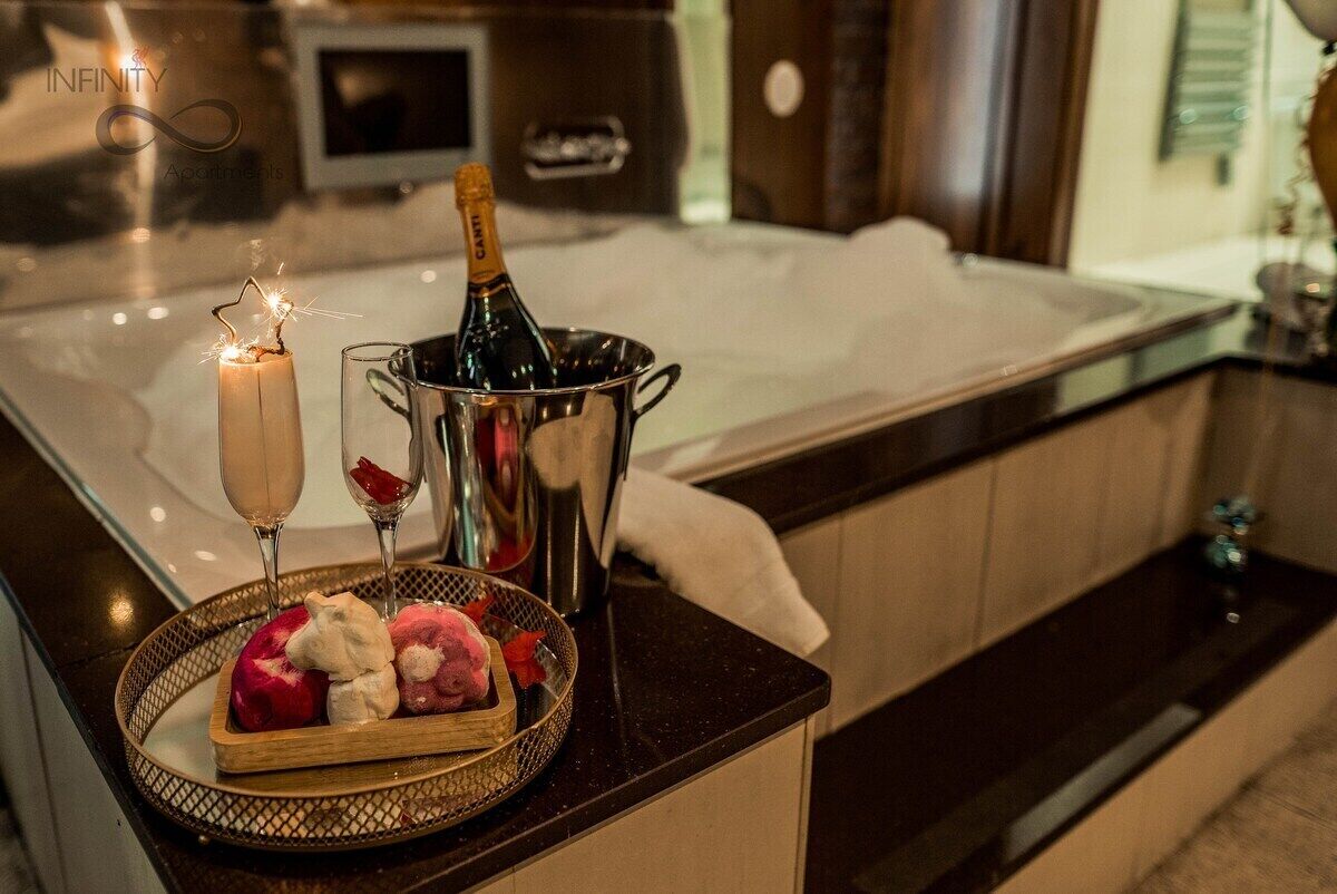 Een luxueuze badkamer met een bad, een champagnefles en een dienblad met desserts.