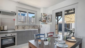 A modern kitchen with stainless steel appliances, a dining table with chairs, and a view of the outdoor area. - 300m from the sea - garden and small pool (Pornic)