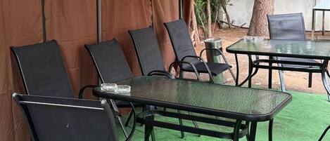 An outdoor seating area with a table and chairs under a canopy, surrounded by greenery.