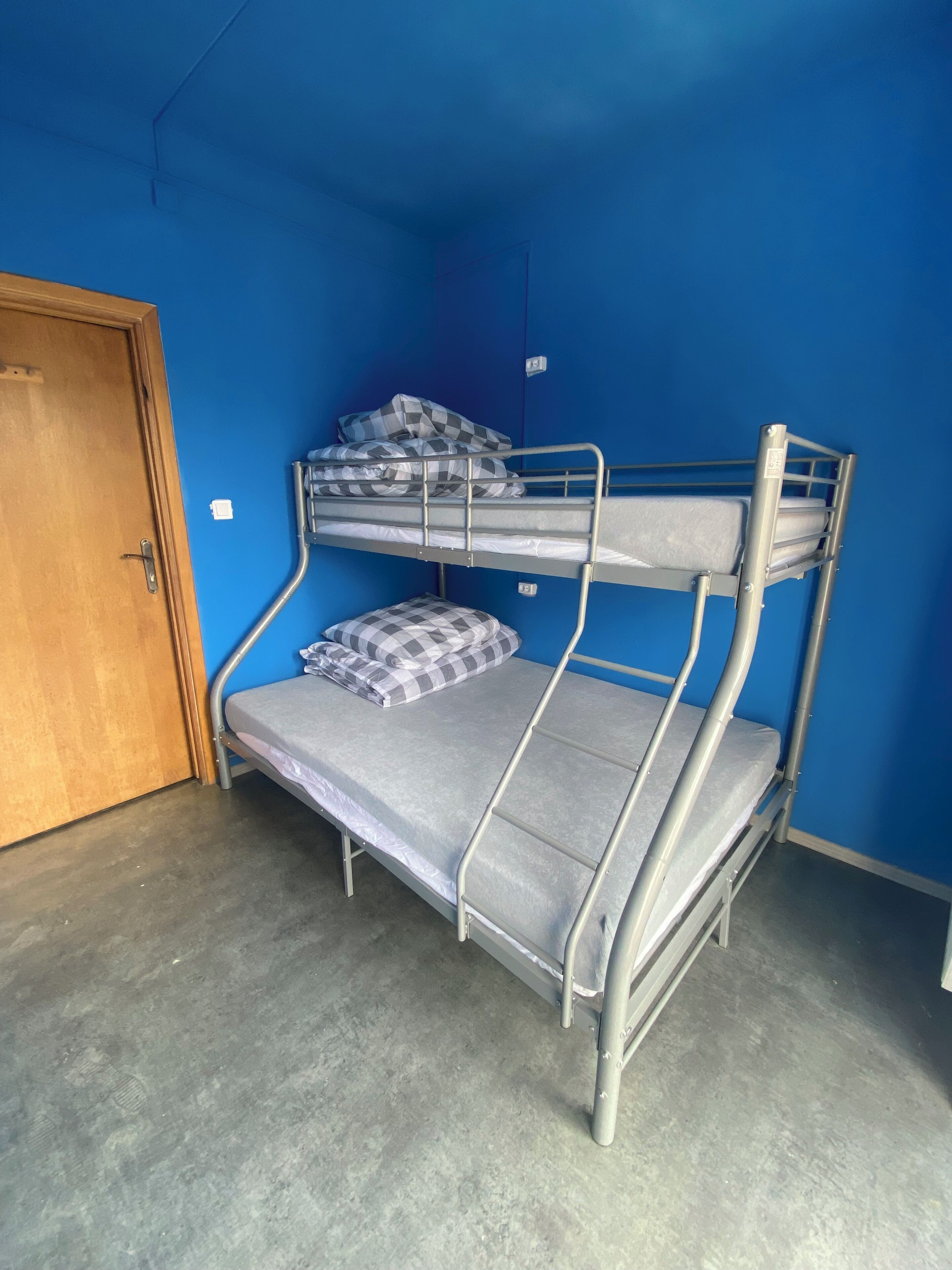 A bunk bed with grey bedding and checkered pillows in a room with blue walls and a wooden door.