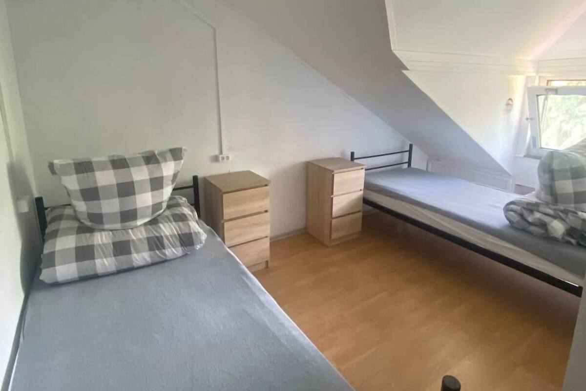 A small, triangular attic bedroom with a single bed, a nightstand, a dresser, and a window providing natural light.