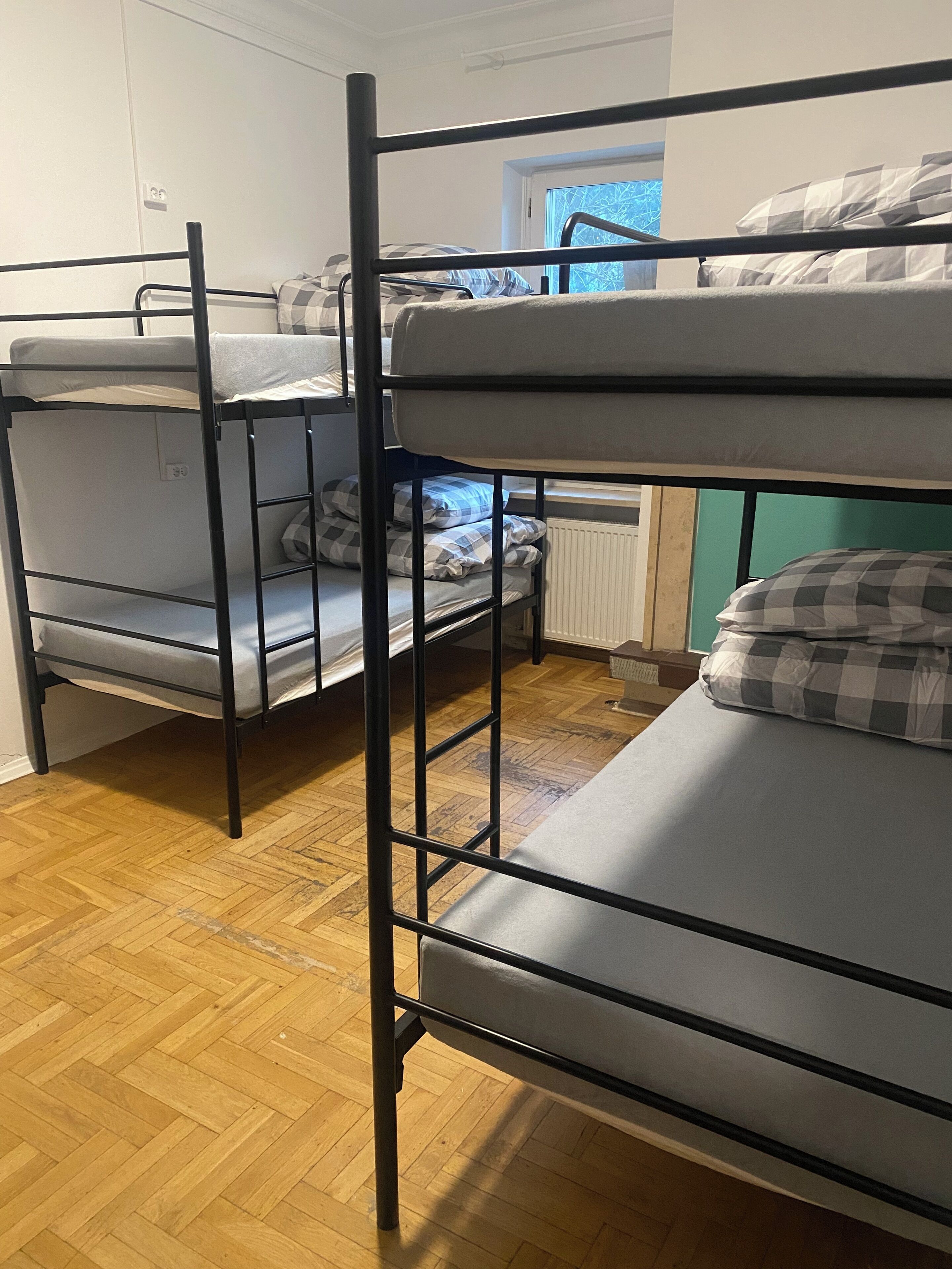 A bunk bed room with a wooden floor, a radiator, and a window with a view.