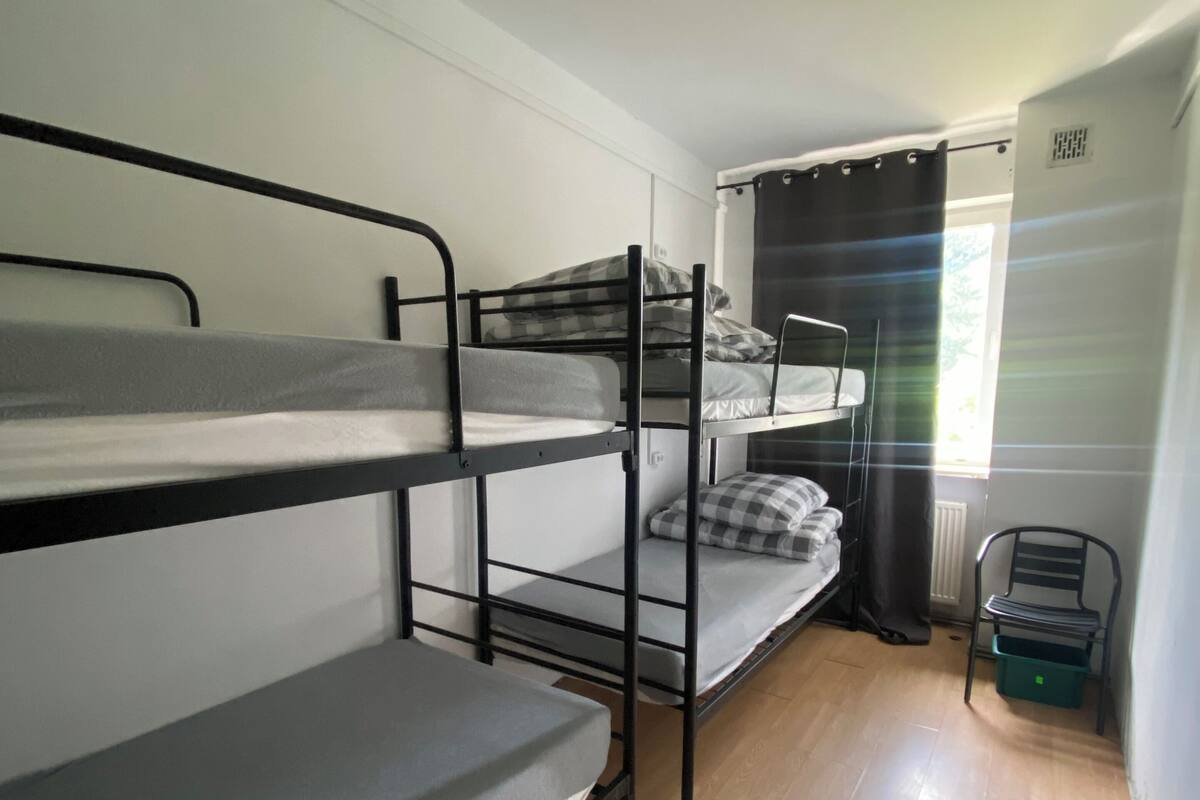 A dormitory room with bunk beds, a chair, and a radiator.