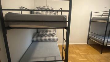 Quarto com beliches, piso de madeira e paredes brancas.