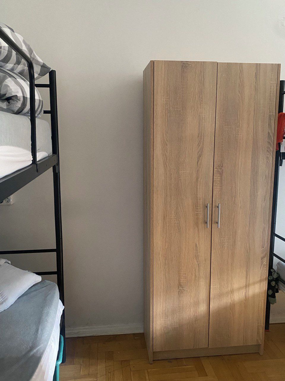 A bunk bed with a grey and white checkered blanket, a wooden wardrobe with two doors, and a wooden floor.