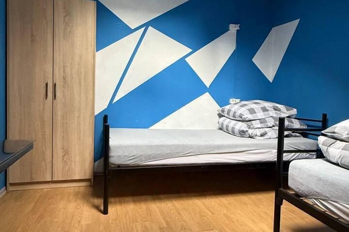 A room with a bed, a wardrobe, and a geometric wall design.